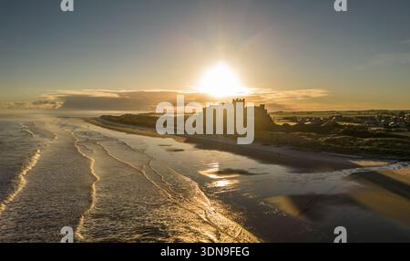 Das berühmte Bamburgh Castle an einem eiskalten Morgen bei Sonnenaufgang, neben dem schneebedeckten Strand in Northumberland, England, von Drohnen eingenommen. Stockfoto