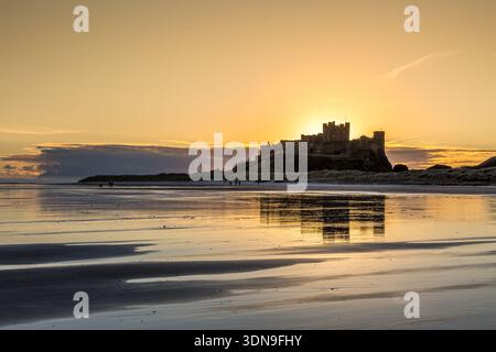 Das berühmte Bamburgh Castle an einem eiskalten Morgen bei Sonnenaufgang, neben dem schneebedeckten Strand in Northumberland, England. Stockfoto
