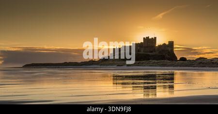 Das berühmte Bamburgh Castle an einem eiskalten Morgen bei Sonnenaufgang, neben dem schneebedeckten Strand in Northumberland, England. Stockfoto