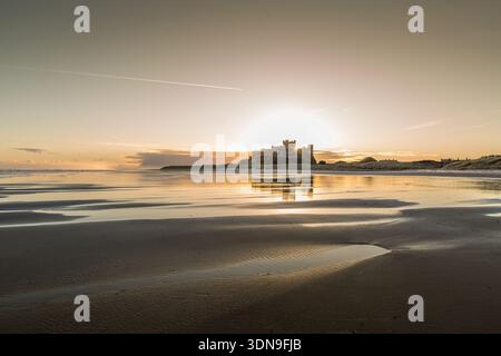 Das berühmte Bamburgh Castle an einem eiskalten Morgen bei Sonnenaufgang, neben dem schneebedeckten Strand in Northumberland, England. Stockfoto