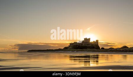 Das berühmte Bamburgh Castle an einem eiskalten Morgen bei Sonnenaufgang, neben dem schneebedeckten Strand in Northumberland, England. Stockfoto