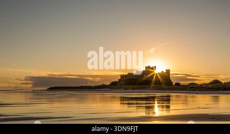 Das berühmte Bamburgh Castle an einem eiskalten Morgen bei Sonnenaufgang, neben dem schneebedeckten Strand in Northumberland, England. Stockfoto