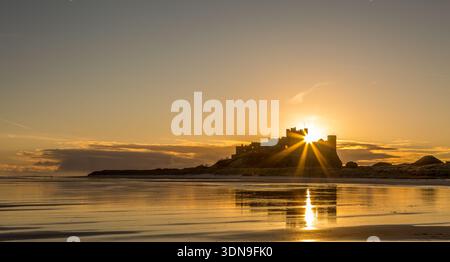 Das berühmte Bamburgh Castle an einem eiskalten Morgen bei Sonnenaufgang, neben dem schneebedeckten Strand in Northumberland, England. Stockfoto