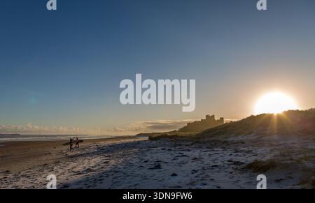 Das berühmte Bamburgh Castle an einem eiskalten Morgen bei Sonnenaufgang, neben dem schneebedeckten Strand in Northumberland, England. Stockfoto