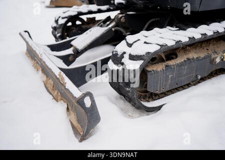 Kompakte Gummikette für Kettenlader mit schneebedecktem Profil und matschigem Unterwagen neben der Befestigung des vorderen Planierschilds, fotografiert auf Winterkonstruktionen Stockfoto