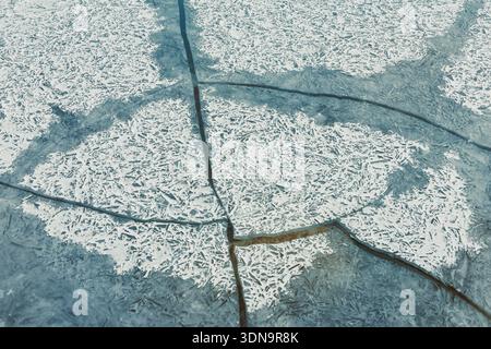Eis bedeckt einen See mit sichtbaren Rissen und Mustern an der Oberfläche. Das kalte Wetter erzeugt Frost und Schnee auf dem Eis. Licht reflektiert von der Oberfläche Stockfoto