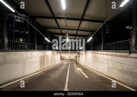 Gut beleuchtete Tiefgaragenrampe in Warschau, Polen, mit moderner Betonarchitektur und klaren Richtungsmarkierungen. Stockfoto