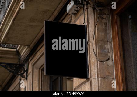 Leeres schwarzes quadratisches Schild, das an der alten Gebäudewand hängt Stockfoto