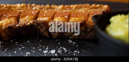 Knusprige Schweinebauchscheiben, mit Salzflocken auf einem dunklen Schieferteller gewürzt Stockfoto