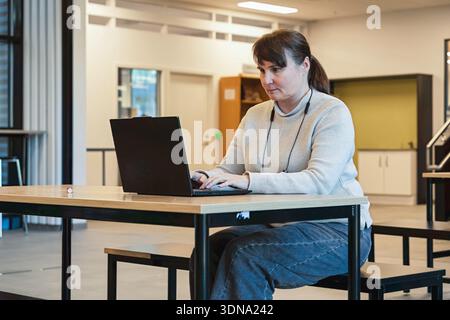 Frau arbeitete an einem modernen Arbeitsplatz mit Laptop, an einem Holztisch, umgeben von einem hellen Innenraum und minimalistischer Einrichtung Stockfoto