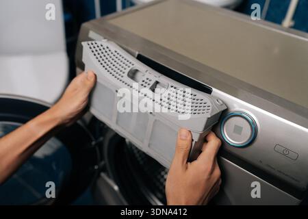 Man entfernt den Flusenfilter aus dem modernen Wäschetrockner, führt routinemäßige Gerätewartung durch, um optimale Leistung und Sicherheit im Haushalt zu gewährleisten, wodurch verhindert wird Stockfoto