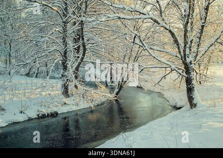 Espoo, Finnland - 31. Dezember 2023: Gefrorener, gewundener Fluss in einem verschneiten Wald bei Sonnenuntergang. Wunderschöne skandinavische Winterlandschaft in Finnland. Stockfoto