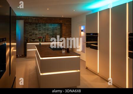Luxuriöses Küchendesign: Nebeneinander liegender Kühlschrank und nahtloser Bodenbelag mit moderner LED-Ambiente-Beleuchtung und Kortenstahl-Arbeitsplatte Stockfoto