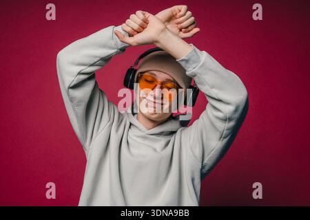Ein Energiegeladener Mann Mit Kopfhörern Und Bunten Brillen, Der Vor Einem Auffälligen Roten Hintergrund Auftritt Stockfoto