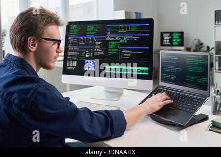 Junger Mann, der im Büro an Computer und Laptop arbeitet Stockfoto