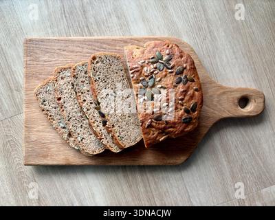 In Scheiben geschnittenes Vollkornbrot mit Kürbis und Sonnenblumenkernen auf Holzschneidebrett. Hausgemachte gesunde Backwaren, Blick von oben, natürliches Licht. Stockfoto