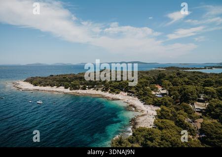 Aus der Vogelperspektive auf das türkisfarbene Wasser, das die zerklüftete Küste küsst, ein Tanz aus tiefem Blau und Erdgrün, Zadar County, Kroatien. Stockfoto