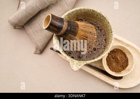 Matcha-Teepulver und -Verquirlen in einer Schüssel, umgeben von traditionellen Zubereitungswerkzeugen Stockfoto