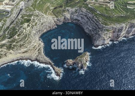 Blick aus der Vogelperspektive auf die zerklüftete Küste, wo türkisfarbenes Wasser auf die imposanten Klippen der Dwejra Bay trifft, was einen dramatischen Kontrast von Texturen und Tönen schafft. Stockfoto