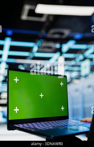 Green-Screen-Laptop, der vom Rechenzentrumsingenieur zur Überprüfung der Gerätediagnose verwendet wird. Mitarbeiter im Serverraum mit Chroma Key Notebook, um Konfigurationen anzupassen und Firmware-Updates anzuwenden Stockfoto