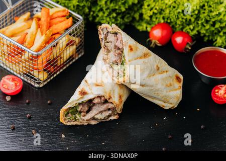 Schweineschawarma-Wraps mit Pommes und Ketchup-Sauce auf schwarzem Tisch, Nahaufnahme Stockfoto