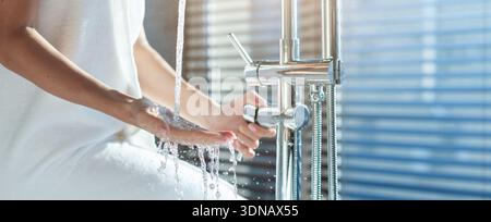 Wasser fließt aus einem Wasserhahn, während eine Person im Badezimmer die Hände wäscht Stockfoto