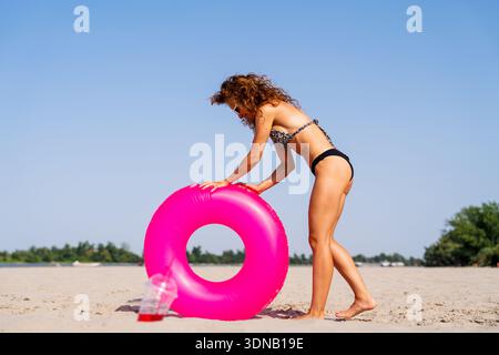 Frau in Bikinis, die im Sommer am Strand mit rosa Floatie Urlaub am Meer genießt Stockfoto