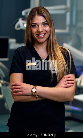 Zuversichtliche weibliche Gesundheitsfachkraft lächelt mit überkreuzten Armen in einer modernen medizinischen Klinik Stockfoto