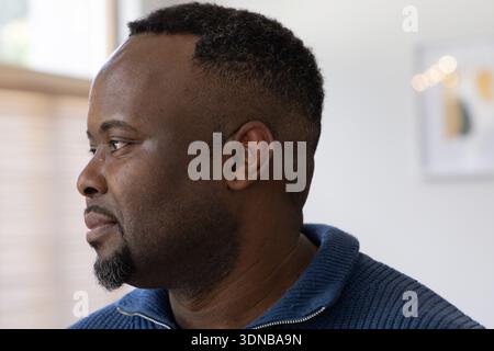 Afroamerikaner blickt nach links, trägt einen blauen Pullover mit Reißverschluss und eine dünne Kette an Fensterläden Stockfoto