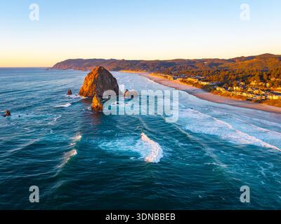 Ein atemberaubender Blick aus der Luft auf Haystack Rock und die Cannon Beach Küste, getaucht in das warme, goldene Licht eines lebendigen Sonnenuntergangs über dem Pazifik Stockfoto