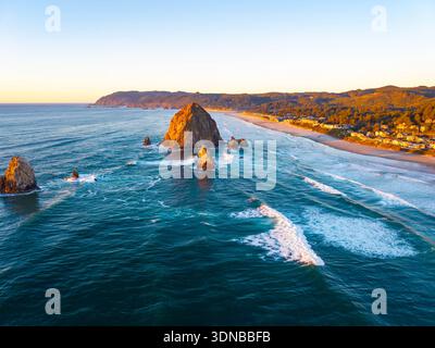 Ein atemberaubender Blick aus der Luft auf Haystack Rock und die Cannon Beach Küste, getaucht in das warme, goldene Licht eines lebendigen Sonnenuntergangs über dem Pazifik Stockfoto