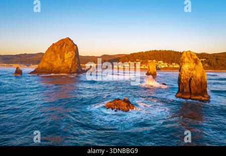 Ein atemberaubender Blick aus der Luft auf Haystack Rock und die Cannon Beach Küste, getaucht in das warme, goldene Licht eines lebendigen Sonnenuntergangs über dem Pazifik Stockfoto