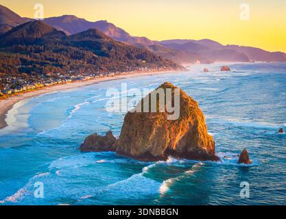 Ein atemberaubender Blick aus der Luft auf Haystack Rock und die Cannon Beach Küste, getaucht in das warme, goldene Licht eines lebendigen Sonnenuntergangs über dem Pazifik Stockfoto