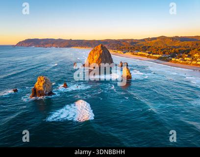 Ein atemberaubender Blick aus der Luft auf Haystack Rock und die Cannon Beach Küste, getaucht in das warme, goldene Licht eines lebendigen Sonnenuntergangs über dem Pazifik Stockfoto