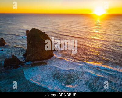 Ein atemberaubender Blick aus der Luft auf Haystack Rock und die Cannon Beach Küste, getaucht in das warme, goldene Licht eines lebendigen Sonnenuntergangs über dem Pazifik Stockfoto