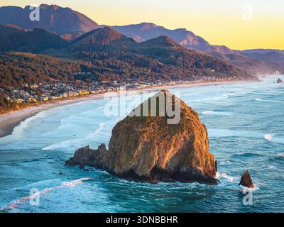 Ein atemberaubender Blick aus der Luft auf Haystack Rock und die Cannon Beach Küste, getaucht in das warme, goldene Licht eines lebendigen Sonnenuntergangs über dem Pazifik Stockfoto