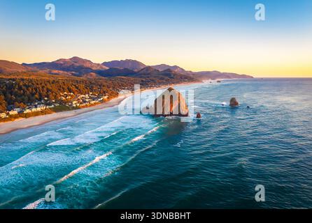 Ein atemberaubender Blick aus der Luft auf Haystack Rock und die Cannon Beach Küste, getaucht in das warme, goldene Licht eines lebendigen Sonnenuntergangs über dem Pazifik Stockfoto