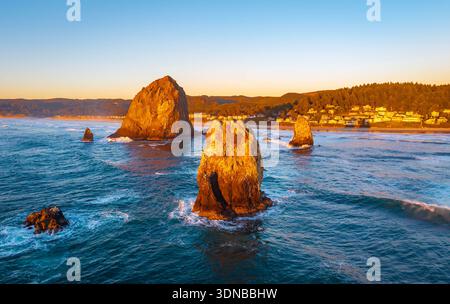 Ein atemberaubender Blick aus der Luft auf Haystack Rock und die Cannon Beach Küste, getaucht in das warme, goldene Licht eines lebendigen Sonnenuntergangs über dem Pazifik Stockfoto