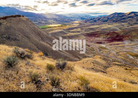 Lebendiger Panoramablick auf die leuchtenden roten, goldenen und schwarzen Schichten von Painted Hills von einem erhöhten Aussichtspunkt am John Day Fossil Beds National Monument bei Sonnenaufgang Stockfoto