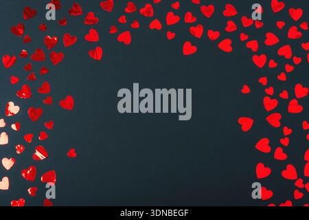 Rote Papierherzen verstreut auf schwarzem Hintergrund mit leerem Mittelraum. Valentinstag-Konzept. Draufsicht, flach. Stockfoto