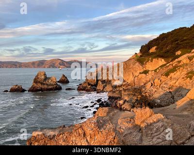 Ein Turm der Golden Gate Bridge ist in der Entfernung hinter dem felsigen Ufer von Land's End zu sehen Stockfoto