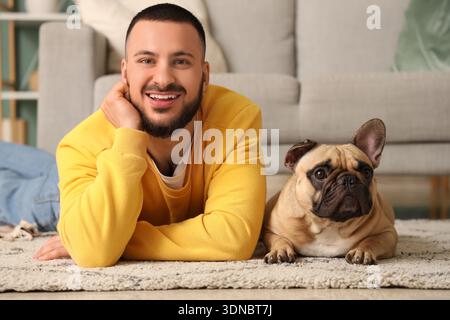 Hübscher junger glücklicher Mann mit süßer französischer Bulldogge, die zu Hause auf dem Boden liegt Stockfoto