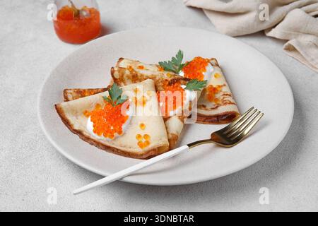 Köstliche Pfannkuchen mit rotem Kaviar und Sauerrahm auf grauem Hintergrund Stockfoto