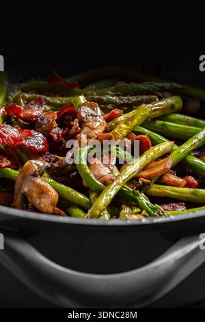 Spargel, Speck und Pilzscheiben in einer Keramikpfanne im Hintergrund gebraten. Saisonales Gemüsekonzept kochen Stockfoto