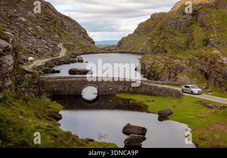 Touristen fahren mit dem Auto über eine Brücke entlang der gewundenen Straße durch die Gap of Dunloe, County Kerry, Irland. Stockfoto