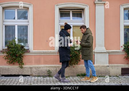 Mann und Frau, die auf dem Bürgersteig stehen und auf das Smartphone schauen. Konzept der gemeinsamen Entscheidungsfindung Stockfoto