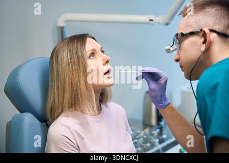 Arzt mit Inspektionsspachtel zur Untersuchung des Rachens des Patienten in der Klinik Stockfoto