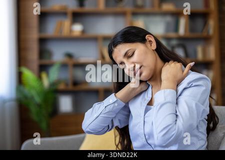 Junge indianerin, die Schulter- und Nackenschmerzen spürt, ihre Muskeln berührt, was auf Stress, Kopfschmerzen, Muskelverspannungen hindeutet. oder Verletzungen beim Entspannen zu Hause Stockfoto