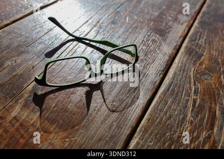 Ein paar grüne Gläser fehlen auf einer Seite, werfen einen Schatten auf rustikales Holz, was an Verlust und Unvollkommenheit erinnert Stockfoto