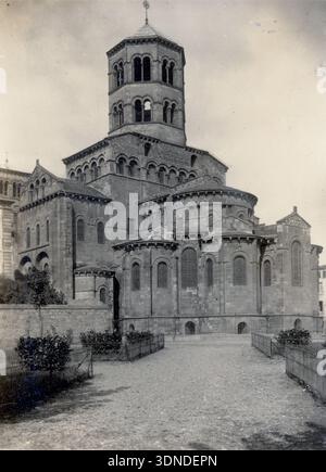 Eine romanische Kirche in Issoire erhebt sich mit einem hohen zentralen Turm, mehrschichtigen Arkaden und mehreren runden Kapellen. Dicke Steinmauern, kleine Bogenöffnungen und gemustertes Mauerwerk bestimmen die Struktur. Ein niedriger Zaun, Sträucher und ein Steinweg umrahmen das Gebäude, während die umliegenden Dächer auf die städtische Umgebung hinweisen. Aus einer Sammlung einzigartiger Fotografien des 20. Jahrhunderts. Amateurfotograf, Schnappschüsse und einige größere in einem einzigen Album, das die Reisen einer Familie in Europa dokumentiert. Stockfoto